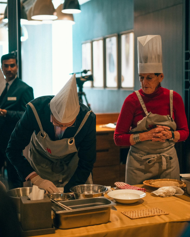 Two chefs in aprons and hats working in a professional kitchen setting.